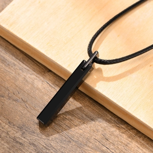 Detail view of a black tungsten steel bar pendant with a black wax rope on wood