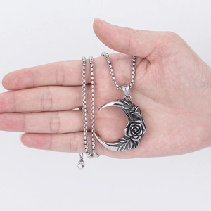 Gothic rose and moon pendant necklace in silver metal held in hand over white background