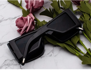 Close-up of black geometric rectangle sunglasses with silver temple details on marble