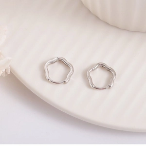 Macro shot of silver wavy ear hoops on a white ceramic plate with soft natural lighting