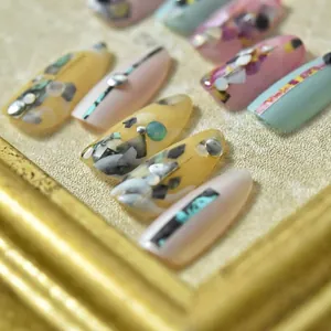 Pastel marble press-on nails with shell accents and metal studs in a gold frame