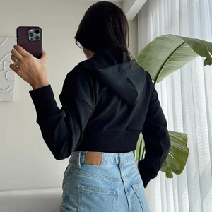 Rear view of a black cropped zip-up hoodie and high-waisted blue jeans in a mirror