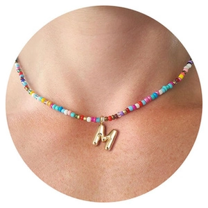 Close-up of a colorful beaded necklace with a golden letter M pendant on a model