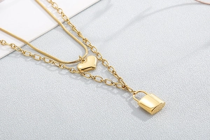 Macro detail of gold double-layer necklace with smooth heart and padlock pendants