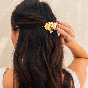 Detail of a golden irregular liquid metal hair clip with textured folds on wavy dark hair