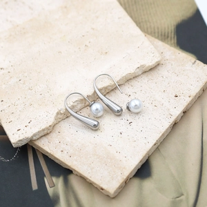 Minimalist silver-tone geometric teardrop pearl earrings on a beige stone display