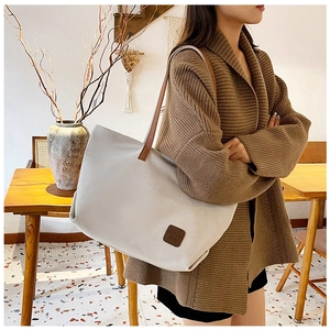 Minimalist canvas tote bag with brown handles worn by model in a warm setting