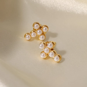 Détail des boucles d'oreilles croix en or 18K avec perles blanches sur soie douce
