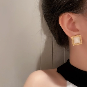 Close-up of a model wearing square opal earrings with a vintage gold textured frame