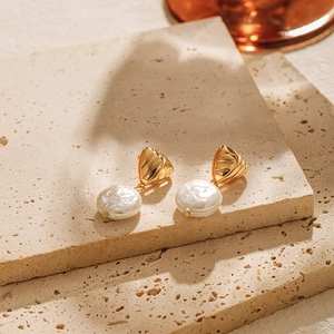 Close-up of geometric gold-plated earrings with baroque pearls on stone texture