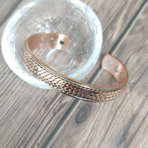 Rose gold magnetic copper bracelet with twisted woven design on a clear glass stand