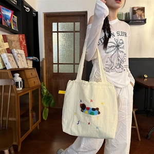 Detail view of yellow canvas tote bag with plush cartoon character and colorful embroidery