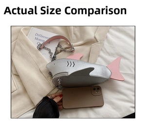 Silver shark shaped crossbody bag with pink fins and metal chain next to mobile phone