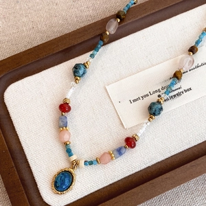 Collier ethnique en perles colorées avec pendentif ovale bleu sur plateau en bois