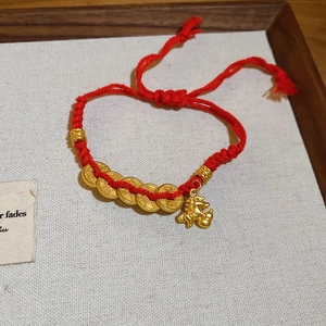Detail of red braided rope bracelet with golden horse charm and five coins on a tray