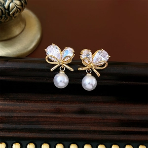 Gros plan de boucles d'oreilles nœud doré avec zircons en cœur et perles blanches
