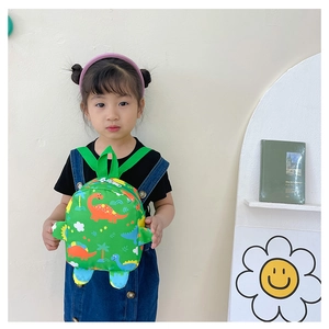 Toddler model wearing green cartoon dinosaur backpack against a minimalist white background