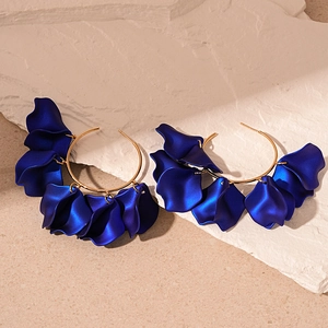 Close-up of matte dark blue flower petal charms on golden hoop earrings set on stone