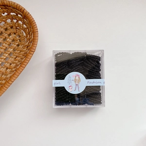 Close-up of small black elastic hair ties packed in a clear box with a cartoon sleeve