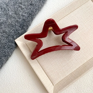 Detailed view of a dark red star-shaped hair claw clip on a beige textured tray