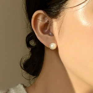 Detail shot of a round pearl stud earring with micro-bead metal edge on a model's ear
