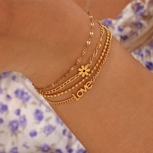 Detail shot of multi-layer gold bracelets with Love charm and daisy pendant on wrist