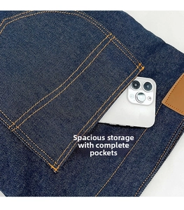 Dettaglio di una tasca in denim blu scuro con cuciture arancioni e uno smartphone bianco