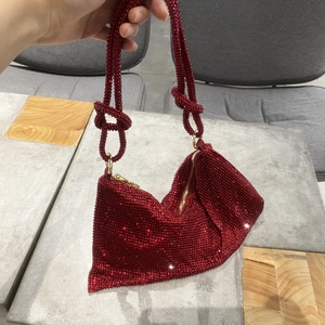 Close-up of sparkling red rhinestone handbag featuring knotted shoulder strap and gold zipper