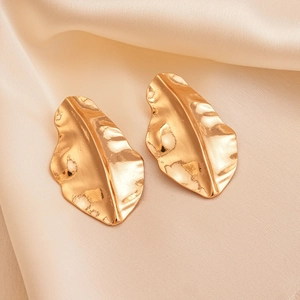 Detailed view of golden irregular leaf earrings on soft beige silk fabric background