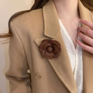 Detail of a dark coffee wool camellia flower brooch on a camel blazer lapel