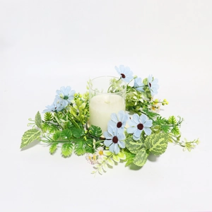 Detailed view of light blue artificial flowers and greenery around a white glass candle holder