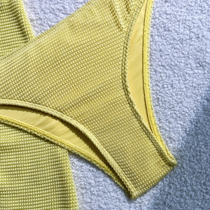 Close-up of yellow seersucker bikini fabric texture and neat stitching on plush background