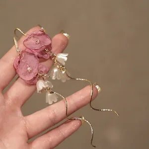 Close-up of handmade pink fabric flower earrings with white lily of the valley tassels