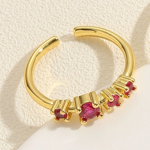 Vue macro de la bague vague plaquée or avec cinq zircons rouges gradués sur fond beige clair