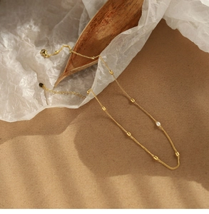 Detailed close-up of 18K gold-plated chain with white pearl and gold bead on warm background