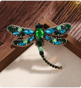 Macro detail of dragonfly brooch featuring emerald-cut green crystal and vintage gold base