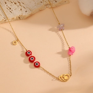 Detail of gold necklace with red evil eye bead, heart pendant and colorful natural stones