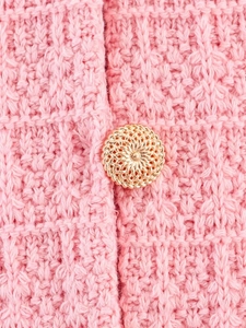 Detailed close-up of pink knit fabric with an elegant hollow gold decorative button