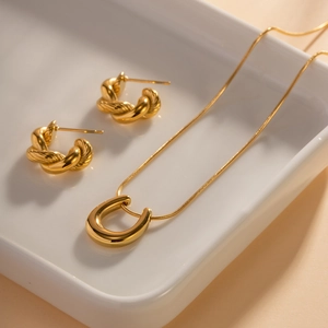 Golden twisted hoop earrings and U-shaped pendant necklace set on a white ceramic tray