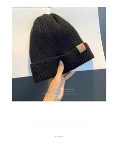 Close-up of black ribbed knit beanie with brown leather logo tag detail