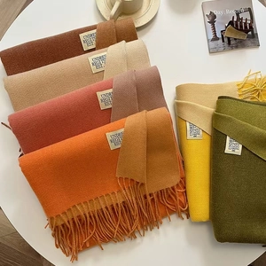 Close-up of fringe tassels and woven brand labels on assorted cashmere-feel scarves