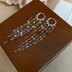 Detail of colorful crystal fringe earrings with silver chain tassels on wood texture