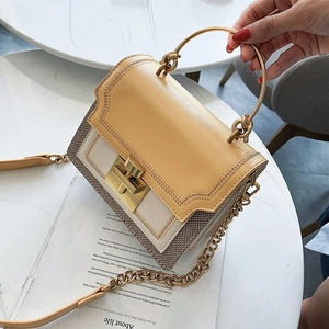 Retro color-block crossbody bag with gold round handle and chain strap on a white table
