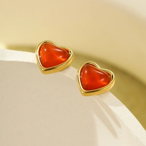 Macro detail of heart-shaped earrings with red stone inlay and gold-plated frames