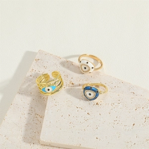 Three-piece set of golden evil eye rings with blue enamel and zircon on stone background