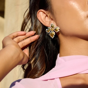 Close-up of model wearing gold flower earrings with white enamel edges and fine texture