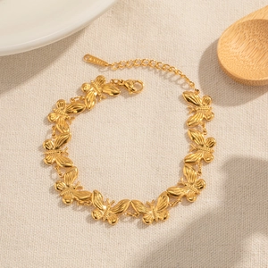 Détail des maillons papillon dorés d'un bracelet en acier inoxydable sur tissu crème
