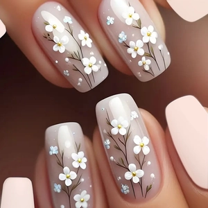 Elegant medium-long press-on nails featuring white floral patterns and golden accents