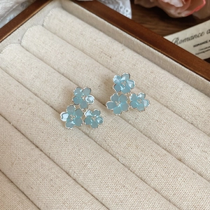 Détail de boucles d'oreilles fleurs en résine bleu clair sur un coffret à bijoux en lin