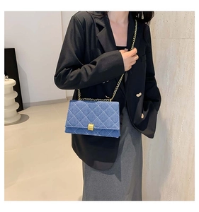 Detail of blue denim quilted handbag with gold chain strap worn by a model